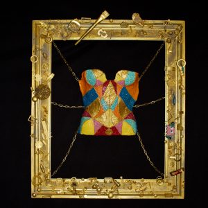 “Tight Corsets of Morality” by Olga Guarch Andreu, papier-mâché corset with inlaid crystals and recycled materials suspended in a golden frame.